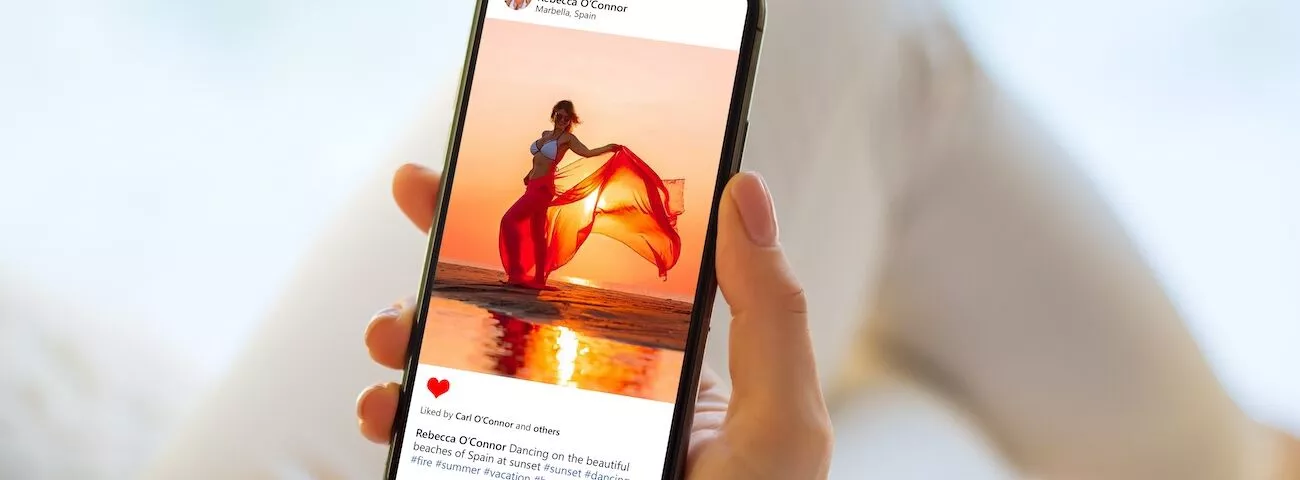 A blogger holding a cell phone with a picture of a woman in a red dress.